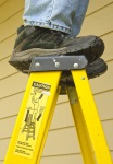 man standing on the top step of a stepladder with caution sticker showing danger