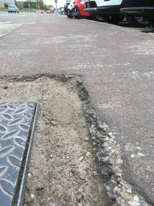 Photo of pavement defect with 1p coin positioned vertically to show scale and height difference